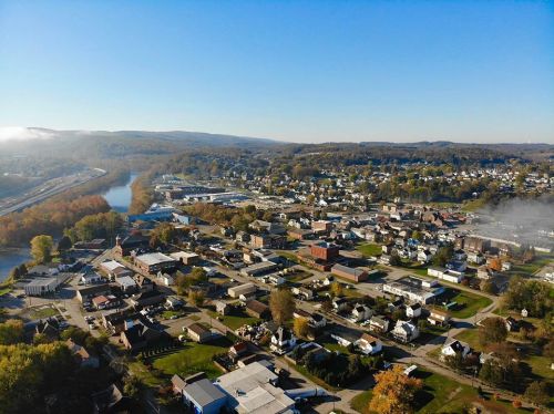 Aerial view of a small town with autumn foliage, a river, and a clear blue sky in the background.