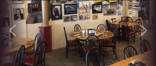 Cozy restaurant interior with wooden tables, black chairs, and framed photos on the walls.
