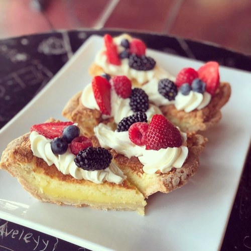 Three fruit-topped tart slices with whipped cream on a white plate, featuring strawberries, blueberries, and blackberries.