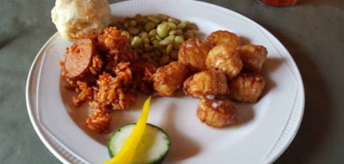 A plate of food featuring rice with sausage, fried plantains, green beans, a biscuit, and cucumber slices.