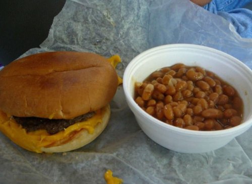 A cheeseburger with melted cheese on a bun next to a bowl of baked beans.