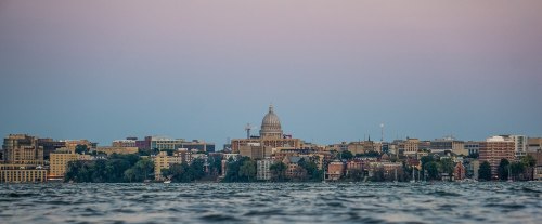 View of a city skyline at dusk, featuring a prominent dome building and water in the foreground.