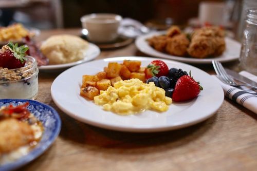 A plate with scrambled eggs, roasted potatoes, strawberries, and blueberries, surrounded by various breakfast dishes.