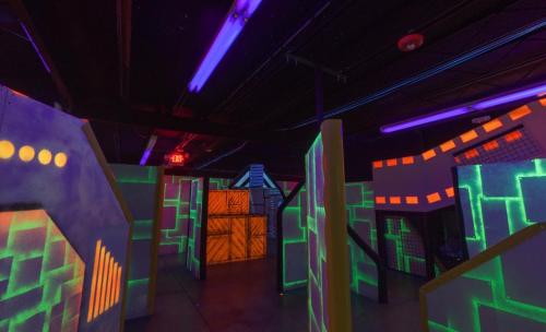A dimly lit laser tag arena with neon walls and glowing obstacles, featuring vibrant colors and a maze-like layout.