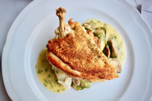 A plated dish featuring crispy chicken, creamy mashed potatoes, Brussels sprouts, and a light sauce.