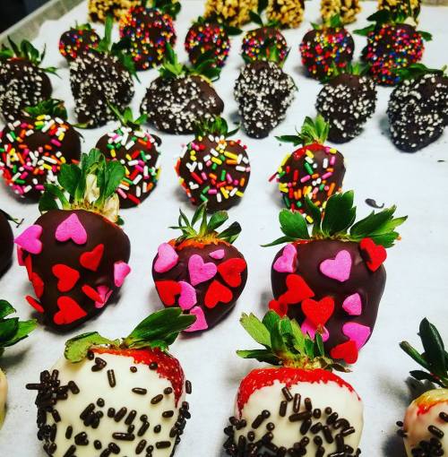 A variety of chocolate-covered strawberries decorated with colorful sprinkles and heart-shaped candies on a tray.
