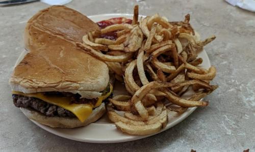 A plate with a cheeseburger on a bun and a side of curly fries, accompanied by ketchup.