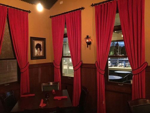 Cozy restaurant interior with red curtains, a framed portrait, and windows revealing an outdoor view.