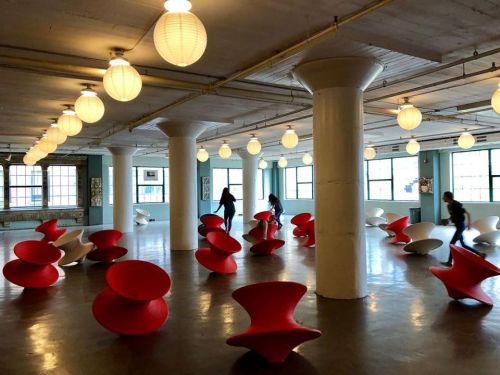 A spacious room with red and white sculptural chairs and people interacting, illuminated by hanging lanterns.