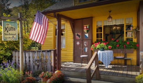 A charming yellow restaurant with an American flag, outdoor seating, and colorful flowers.
