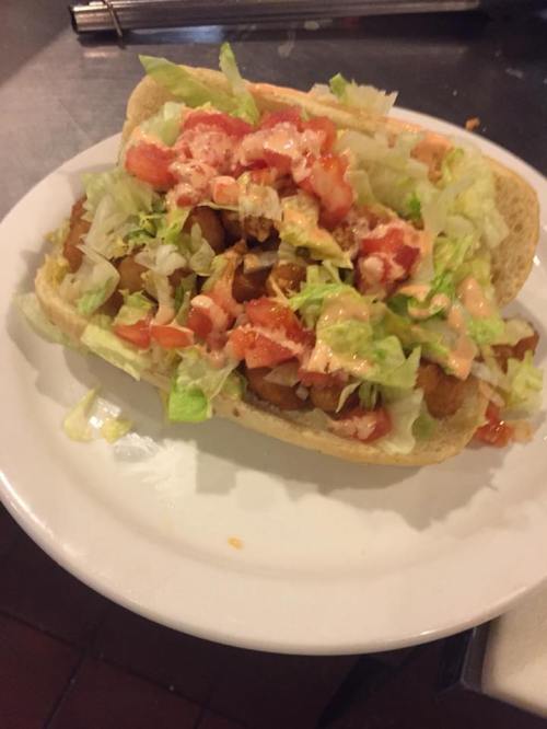 A large sandwich filled with lettuce, tomatoes, and sauce on a toasted bun, served on a white plate.