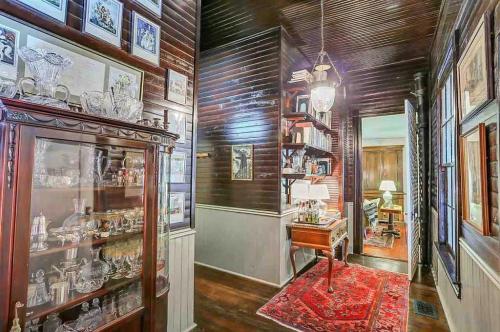 A vintage hallway featuring dark wood paneling, a bookshelf, decorative glassware, and a red area rug.
