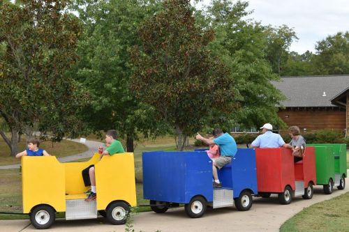 A colorful train ride with children and adults enjoying a fun outing in a park setting.