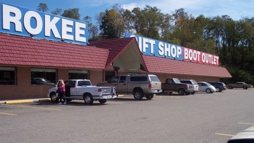 A gift shop and boot outlet with a red roof, featuring parked vehicles and trees in the background.