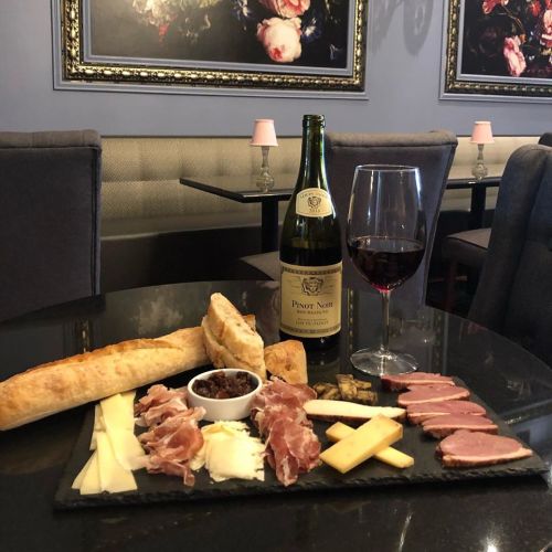 A gourmet spread featuring cured meats, cheeses, bread, olives, a bottle of Pinot Noir, and a glass of red wine.