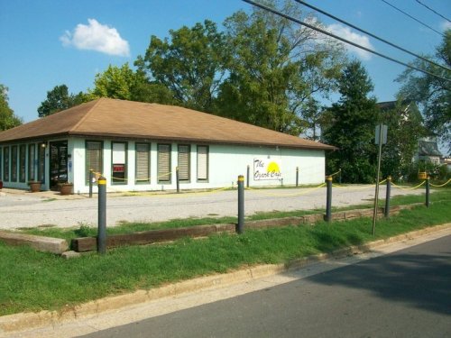A single-story building with a brown roof and green walls, surrounded by grass and trees, with a sign reading "The Guest Cafe."