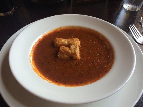 A bowl of tomato soup with two pieces of bread floating on top, served in a white dish on a dark table.