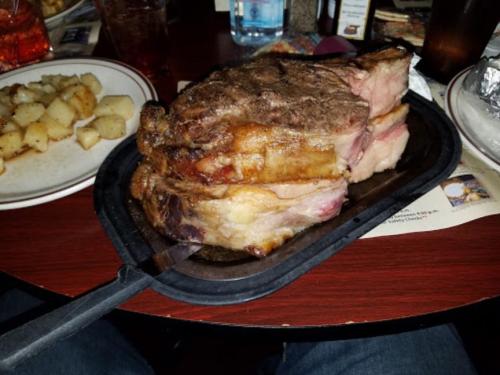 A large, juicy prime rib served on a sizzling platter, with a side of roasted potatoes on a table.