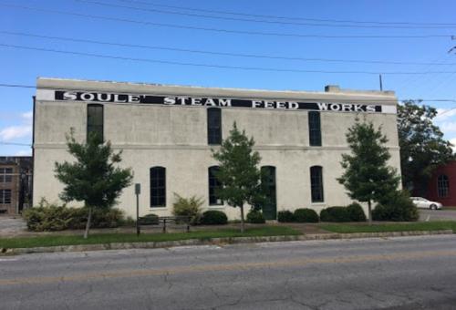 Historic building with "Soule Steam Feed Works" painted on the side, surrounded by trees and a clear blue sky.
