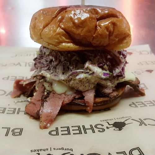 A close-up of a sandwich with sliced meat, coleslaw, and sauce on a toasted bun, served on a paper wrapper.