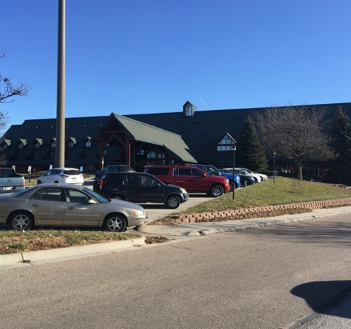 A parking lot with several cars in front of a large building under a clear blue sky.