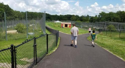 A pathway through a grassy area with enclosures, featuring two adults and a child walking in the distance.