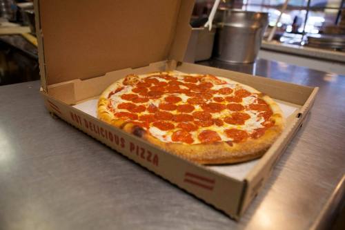 A pepperoni pizza in an open box on a countertop, with a kitchen setting in the background.