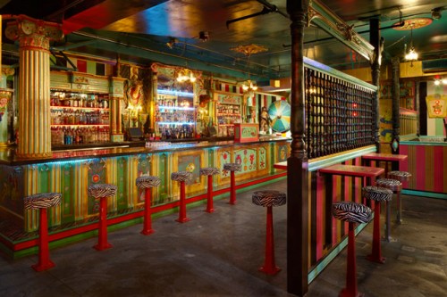 Colorful bar interior with vibrant decor, striped walls, and zebra-patterned stools. Brightly lit and inviting atmosphere.