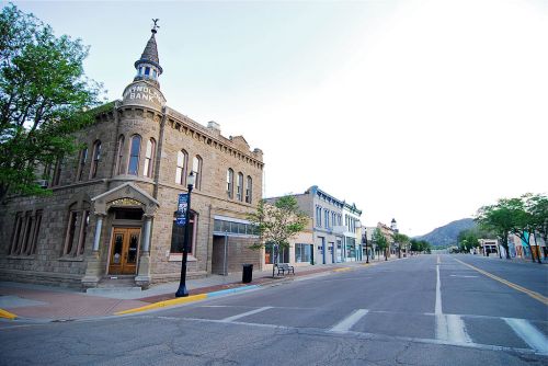 Historic bank building on a quiet street, flanked by charming storefronts and trees under a clear sky.