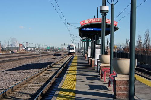 A train approaches Oxford Station, with a platform and signage indicating southbound service. Clear blue sky above.