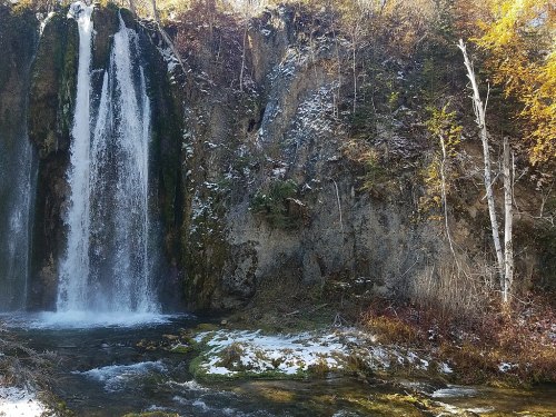 A serene waterfall cascading down a rocky cliff, surrounded by autumn foliage and a tranquil stream below.