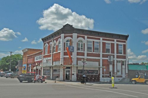 Historic brick building at a street corner, featuring large windows and a colorful awning, under a partly cloudy sky.