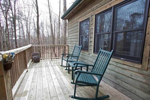 Two green rocking chairs on a wooden deck surrounded by bare trees in a tranquil outdoor setting.