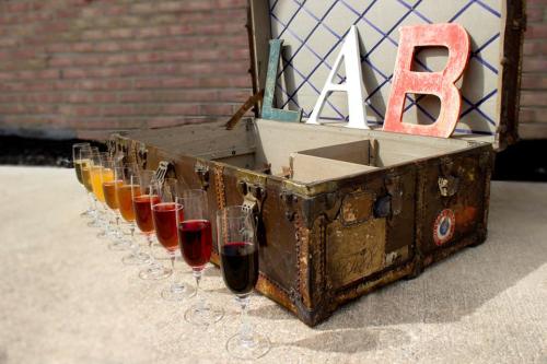 An open vintage suitcase displays colorful drinks in glasses lined up in front, with decorative letters "L," "A," and "B."