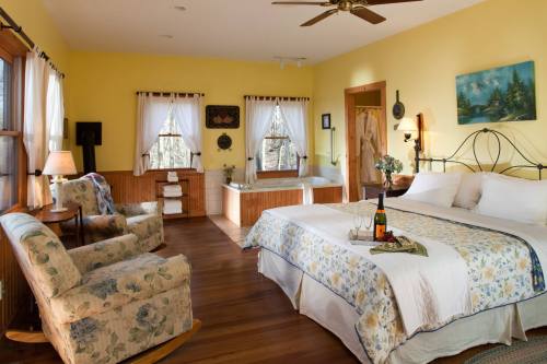 Cozy bedroom with a queen bed, floral decor, seating area, and a jacuzzi, featuring warm yellow walls and natural light.