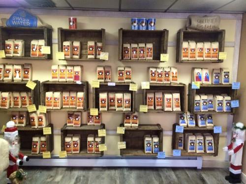 A wall display of coffee bags on wooden shelves, with festive decorations and labels in a cozy shop setting.