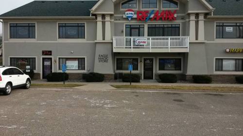 Exterior view of a commercial building featuring RE/MAX and Eagle Magic Store signs, with parking in front.