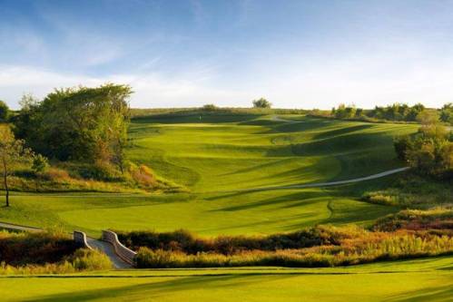 A scenic view of a lush green golf course with rolling hills and a clear blue sky.