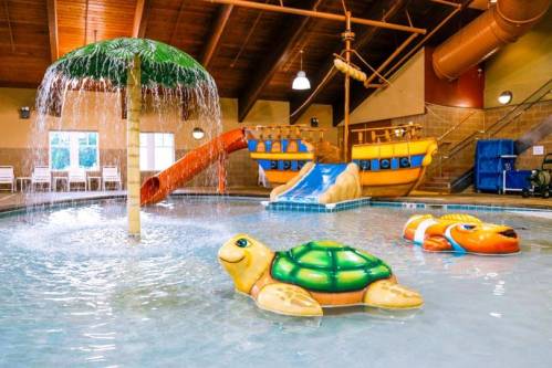 Indoor water play area featuring a palm tree fountain, a slide, and colorful inflatable turtles and fish.