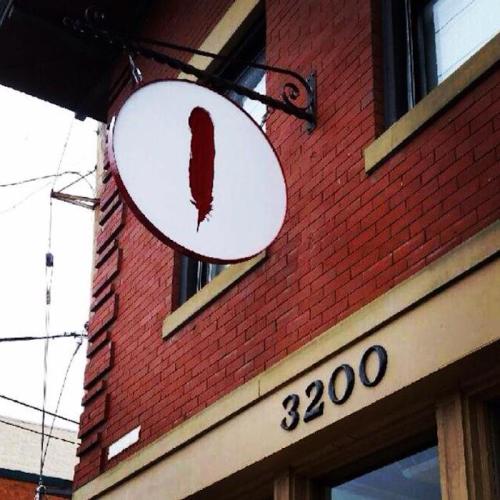 A round sign with a red feather hangs above a building's entrance, featuring the number 3200 on the wall below.