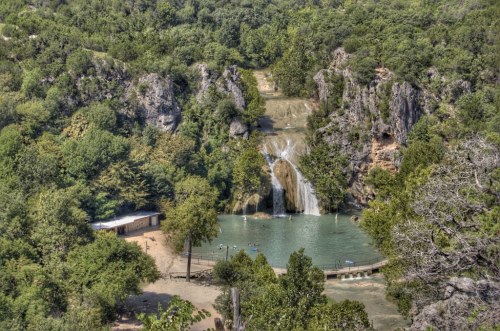 A scenic view of a waterfall cascading into a turquoise pool, surrounded by lush greenery and rocky cliffs.