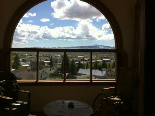 A scenic view through a large arched window, showcasing mountains and a town under a blue sky with fluffy clouds.