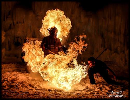 A performer breathes fire, creating a dramatic flame display against a snowy backdrop.