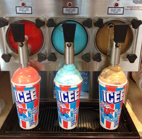Three colorful ICEE drinks in large cups, with red, blue, and brown flavors, dispensed from a machine.