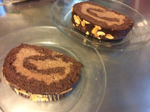 Two slices of chocolate roll cake with a creamy filling, garnished with almond slices, on clear glass plates.