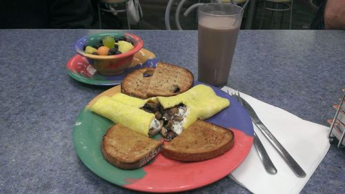 A colorful plate with an omelet, toast, and a side of fruit, accompanied by a glass of chocolate milk.