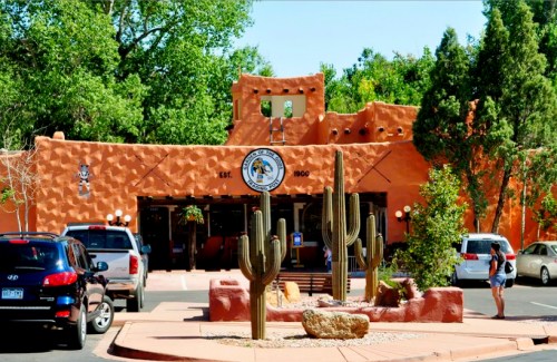 A southwestern-style building with a terracotta exterior, surrounded by cacti and trees, featuring a sign that says "Est. 1900."