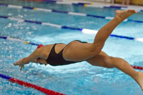 A swimmer diving into a pool, captured mid-air with water splashing around.