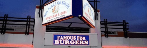 Sign for "Win Place or Show Sports Bar & Grill," featuring "Famous for Burgers" in bright lights at dusk.