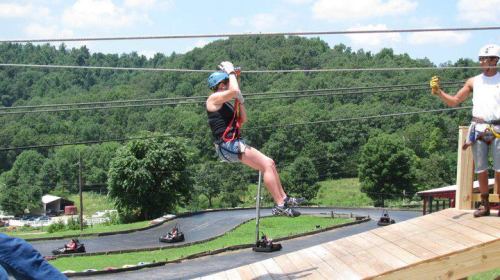 A person zip-lining over a scenic landscape, with another individual preparing to assist on the platform.